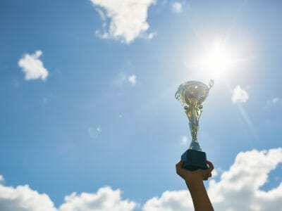 Hand Holding Golden Trophy Against Blue Sky