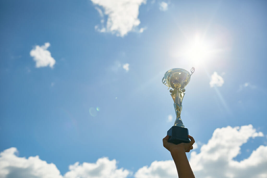 Hand Holding Golden Trophy Against Blue Sky